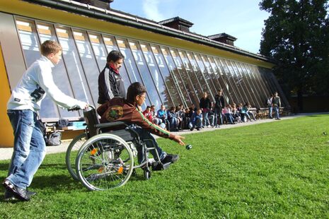 Junge im Rollstuhl spielt mit anderen Kinder Boule